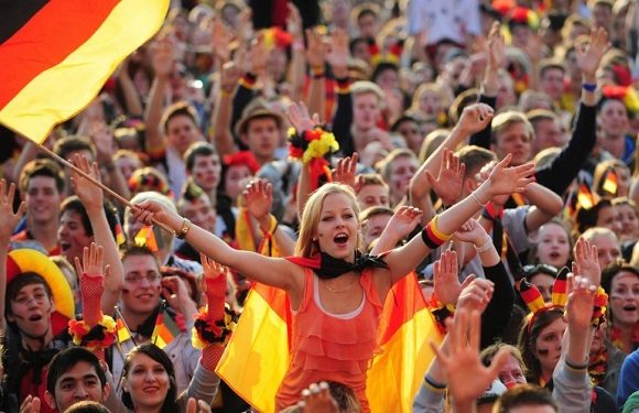 A crowd, many with German flags, enthusiastically watch a likely football event.