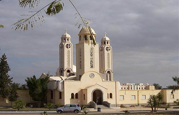 An image of a beige church with two tall bell towers and a cross on top, under a partly cloudy sky.