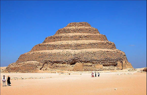 A group of people walking near the base of the Step Pyramid of Djoser under a clear blue sky.