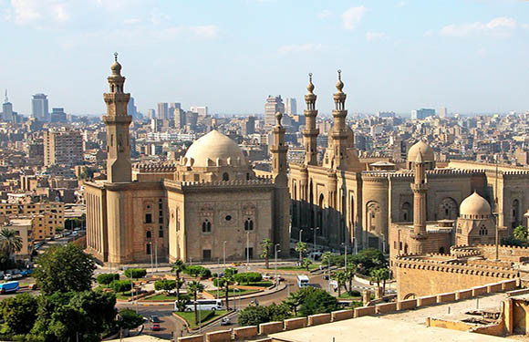 A panoramic view of a historic cityscape with multiple domed and minareted buildings, under a clear sky.