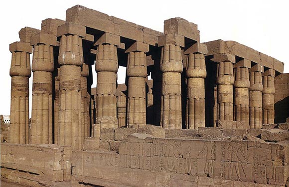 A weathered ancient Egyptian temple with hieroglyph-decorated columns under a clear, sunny sky.