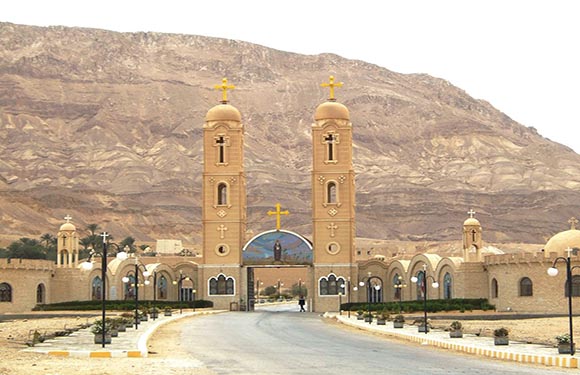 A church with two tall bell towers in front of a mountainous backdrop.