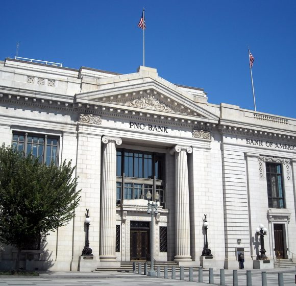 A photo shows a classical building with "PNC Bank" written above the entrance, and two flags flying above.