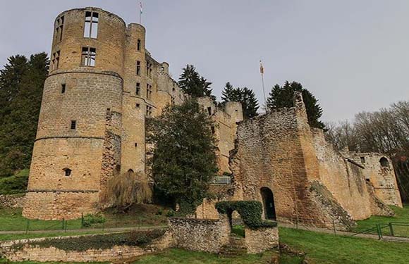 A photo shows an old stone castle with a circular tower, surrounded by wall remnants, trees, and a cloudy sky.