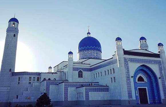 A mosque with a large blue dome and two tall minarets against a clear sky.