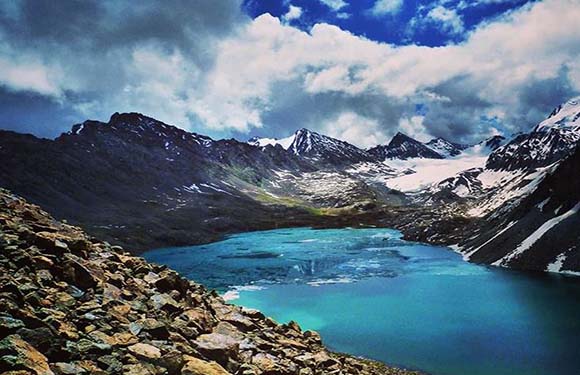 A scenic view of a turquoise lake surrounded by rugged mountains under a cloudy sky.