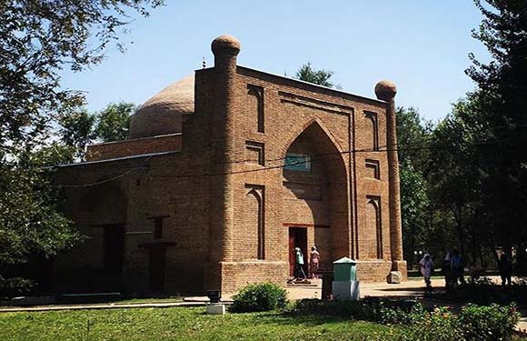 A small brick building with a dome and an arched entrance surrounded by trees.