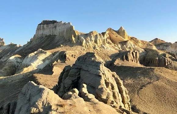 A landscape featuring eroded rock formations and cliffs under a clear blue sky.