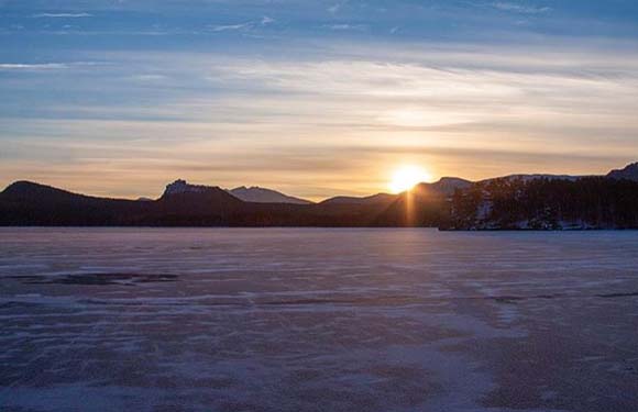 Sunset over a frozen landscape with mountains in the background and a clear sky.