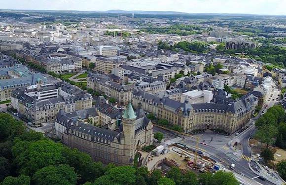 Aerial view of a city with historic buildings and streets, trees scattered throughout, and overcast skies above.