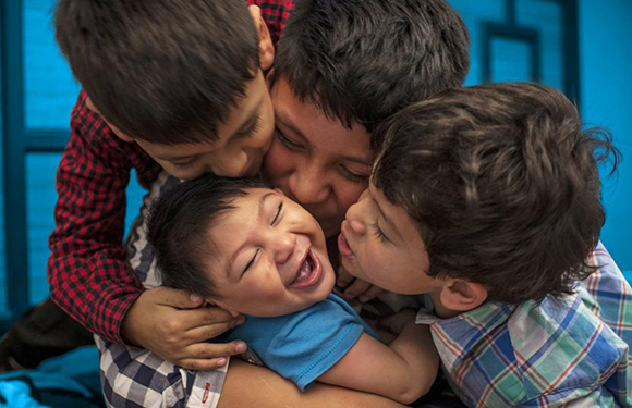 Three kids are happily hugging and kissing a person against a blue wall, enjoying a loving moment.