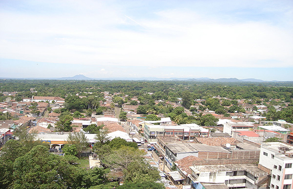 Aerial view of a small town with low-rise buildings, streets, and greenery, under a partly cloudy sky.