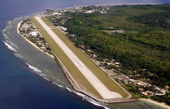 Aerial view of a narrow runway adjacent to a coastline with surrounding vegetation and buildings.