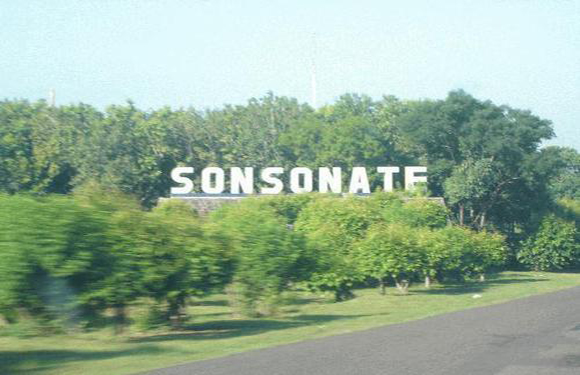 A blurry image of large white letters spelling "SONSONATE" on a green hillside beside a road.