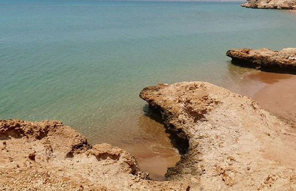 A coastal landscape with sandy cliffs and calm blue water.