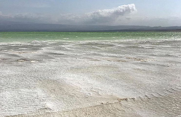 A shallow body of water with ripples on the surface, under a cloudy sky with land visible in the distance.