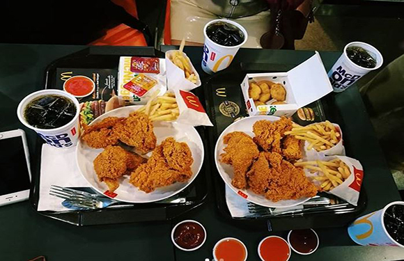 A tray of fast food including fried chicken, fries, nuggets, and soft drinks on a table.