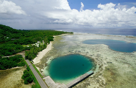 Aerial shot of a coast with two blue water bodies, greenery, and a road parallel to the shoreline.