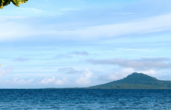 A scenic view of a calm sea with a mountain in the background under a partly cloudy sky.