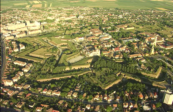 Aerial view of a town with buildings, streets, and green areas during daylight.