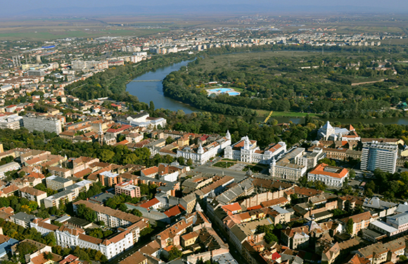 Aerial view of a city with buildings, streets, and a river curving through the landscape.