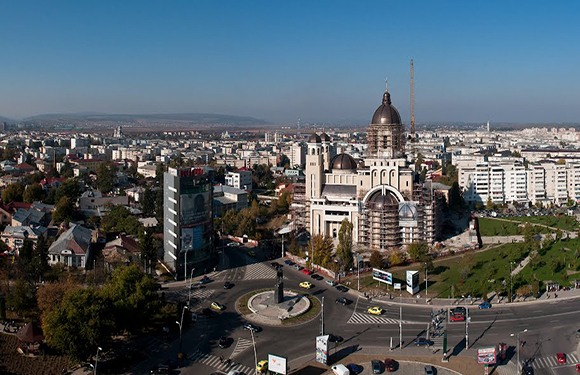 Aerial view of a cityscape with buildings, roads, and a roundabout, under a clear sky.