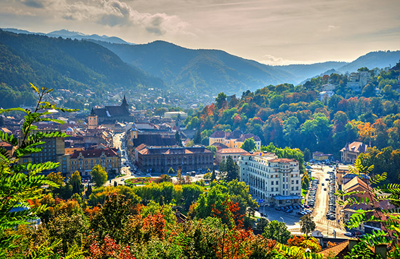 A scenic view of a town nestled in a valley with surrounding forested hills and mountains under a partly cloudy sky.