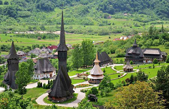 A scenic view of a traditional village with distinctive wooden churches featuring tall spires, surrounded by lush greenery and hills.