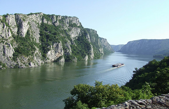 A boat navigates a river in a narrow valley with steep cliffs, surrounded by lush greenery.