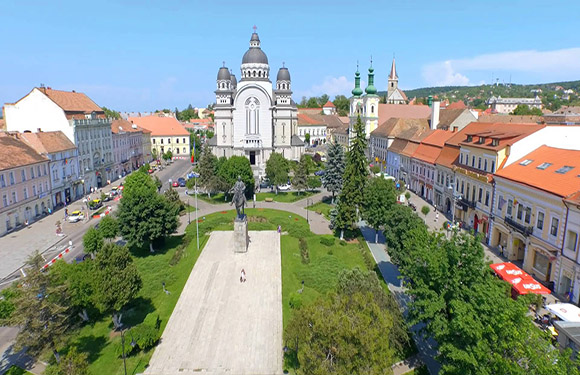 Aerial shot of a town square featuring a domed church, European-style buildings, trees, under a clear blue sky.