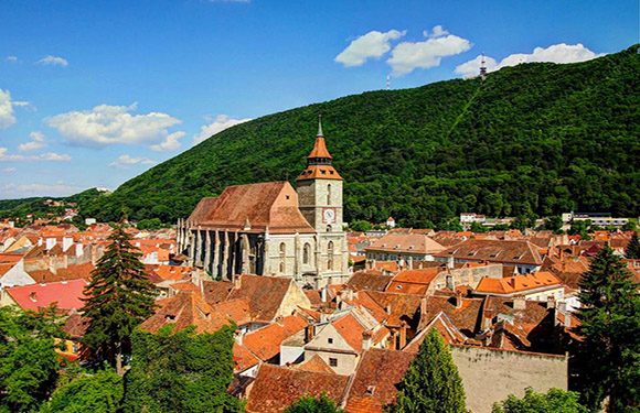 Aerial view of a historic town with red-roofed buildings, a large church, surrounded by green hills.