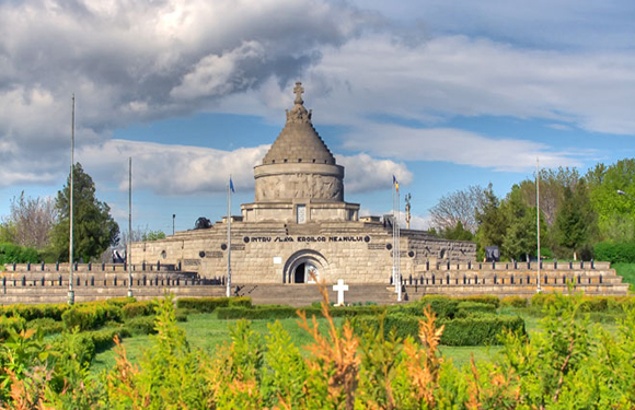 A historical monument with a large dome and sculptures, surrounded by greenery under a partly cloudy sky.