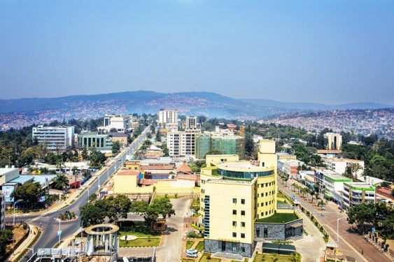 Aerial view of a cityscape with buildings, roads, and vegetation under a clear sky.