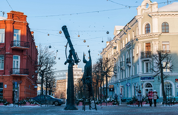 A street view with a unique sculpture of a large gun with a knotted barrel, buildings on either side, and a clear blue sky.