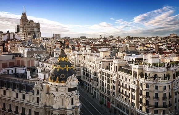 A panoramic view of a cityscape with historic European-style buildings under a blue sky with scattered clouds.