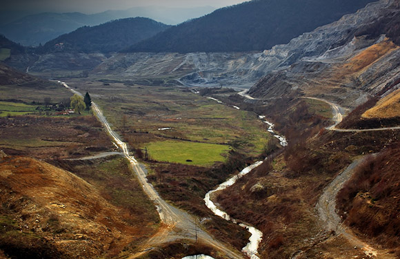 A winding river flows through a valley with brown and green vegetation under a cloudy sky.