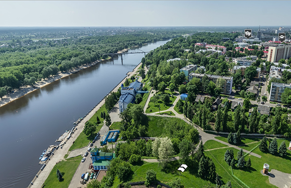 Aerial view of a river flowing through a green landscape with buildings and pathways on its banks under a clear sky.