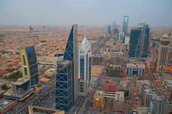 Aerial view of a modern cityscape with high-rise buildings and a busy street, under a hazy sky.