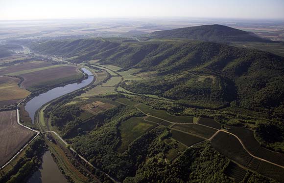 Aerial view of a winding river flowing through a lush landscape with hills, fields, and patches of forest.