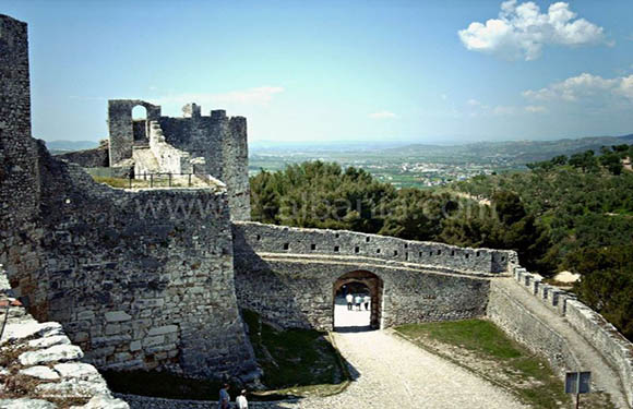 Stone fortress walls and towers on a hill with a view of a distant landscape under a partly cloudy sky.