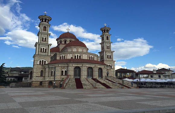 A photo of a large church with multiple domes and bell towers, situated in a spacious square with a partly cloudy sky overhead.