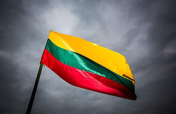 A flag with horizontal stripes of yellow, green, and red against a cloudy sky background.