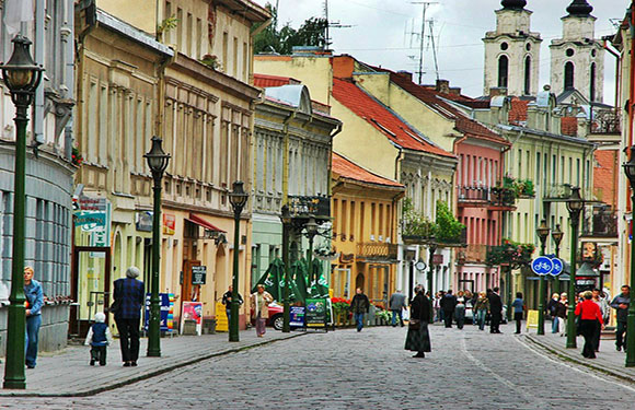 A colorful street scene with historical buildings, pedestrians walking, and a cloudy sky.