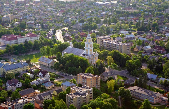 Aerial view of a town with dense building structures, featuring a prominent church with a tall spire, surrounded by greenery.