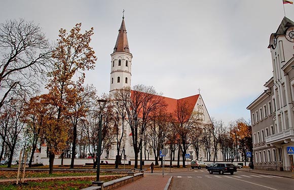 Autumn street view featuring bare trees, a historic church with a tall spire, parked cars, and a cloudy sky.