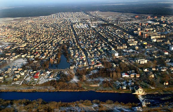 Aerial view of a crowded town near water, with urban landscape transitioning to rural in the distance.