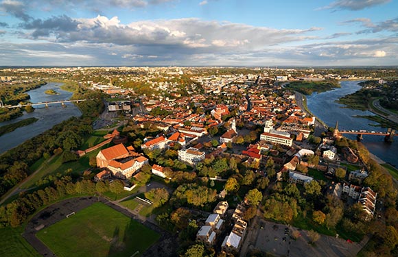 Aerial view of a historic city with dense buildings and a river running through it, under a partly cloudy sky.