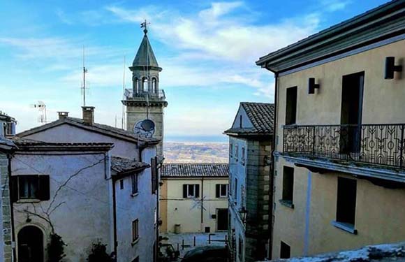 A picturesque view of a quaint old town with historic buildings and a bell tower, under a clear sky.