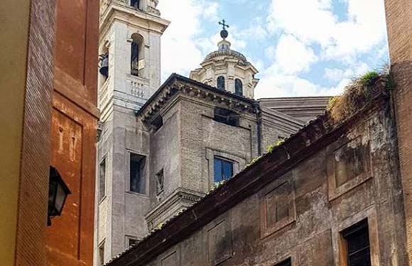 An image of an old church with a bell tower, viewed from a narrow street between buildings.