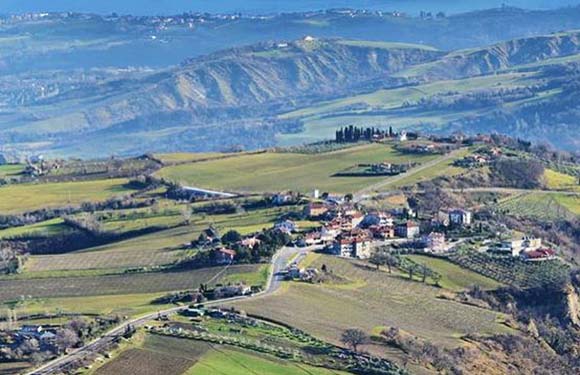 Aerial view of a rural landscape with rolling hills, fields, and a small village with buildings clustered together.